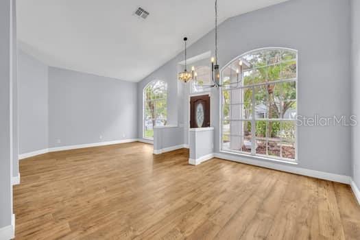 An empty room with light wood flooring, vaulted ceilings, a chandelier, and large arched windows — 1913 MAGIES COURT, OVIEDO, FL
