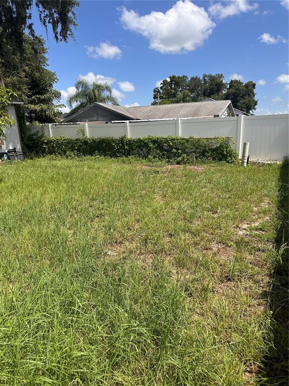 A grassy backyard features a white vinyl privacy fence and mature trees under a blue sky — 8848 OAK CIRCLE, TAMPA, FL
