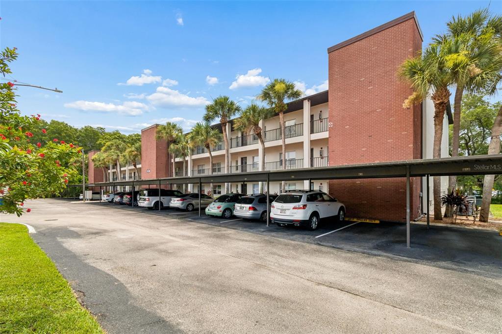 A three-story brick apartment building features a covered parking area with several parked cars — 2438 ENTERPRISE ROAD UNIT 25, CLEARWATER, FL