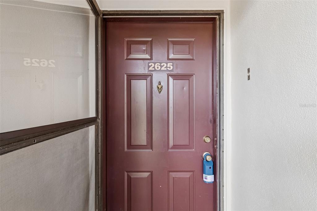 A maroon front door with the number 2625 is visible next to a screen door — 2438 ENTERPRISE ROAD UNIT 25, CLEARWATER, FL