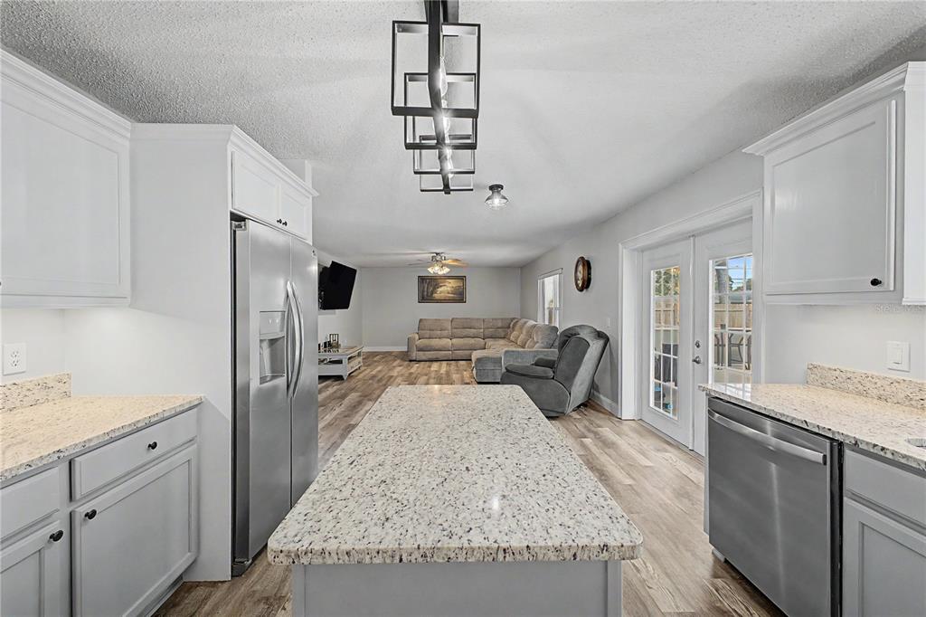 A kitchen with a granite island and stainless steel appliances opens into a living area — 1382 LARKIN ROAD, SPRING HILL, FL