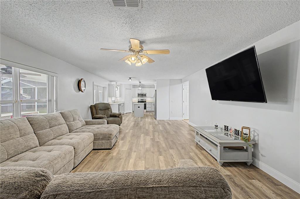 A living room with light wood-look flooring, a sectional sofa, and a wall-mounted television — 1382 LARKIN ROAD, SPRING HILL, FL