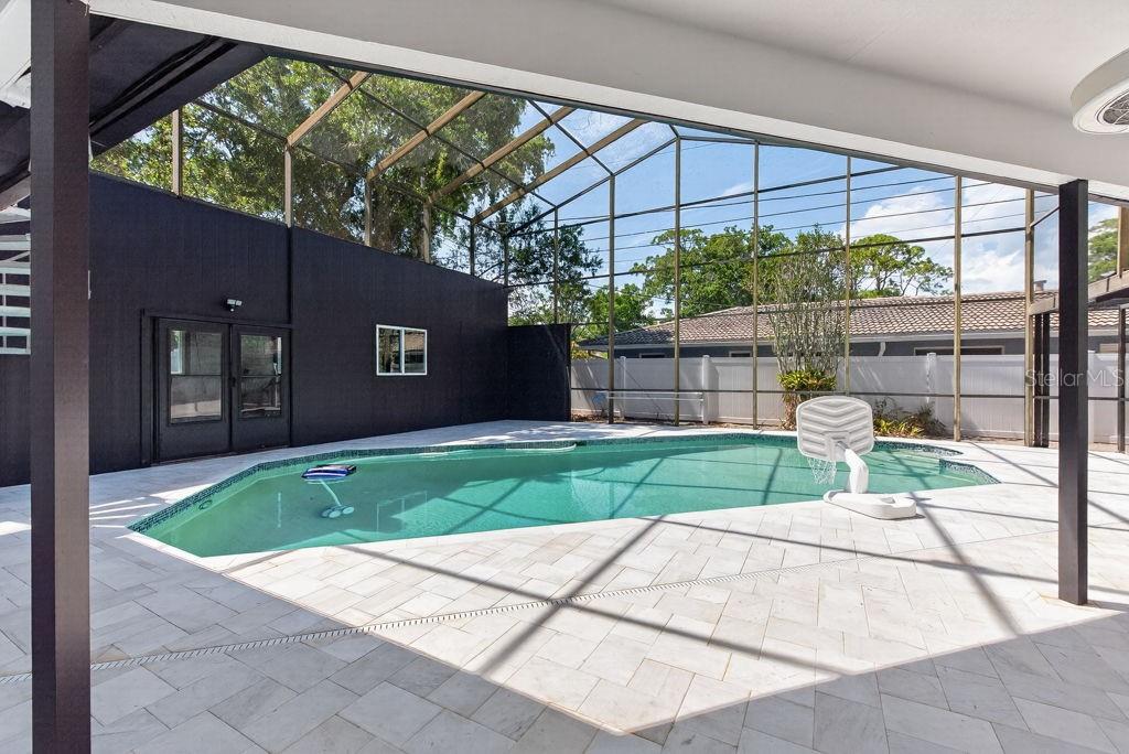 A screened-in pool area features light-colored pavers and a dark accent wall — 1461 87TH AVENUE N, ST PETERSBURG, FL