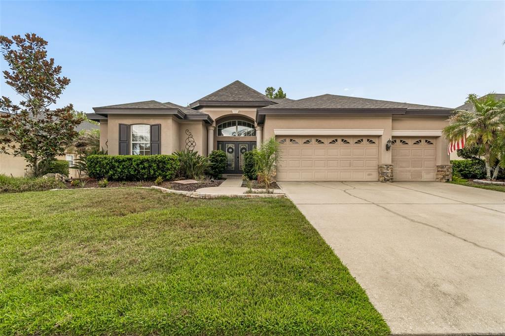 A single-story suburban house with a tan stucco exterior, a three-car garage, and a lawn — 23305 GRACEWOOD CIRCLE, LAND O LAKES, FL
