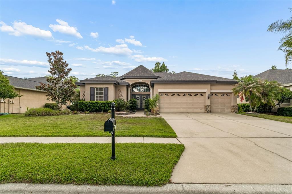 A single-story suburban house with a tan stucco exterior, a three-car garage, and a lawn — 23305 GRACEWOOD CIRCLE, LAND O LAKES, FL