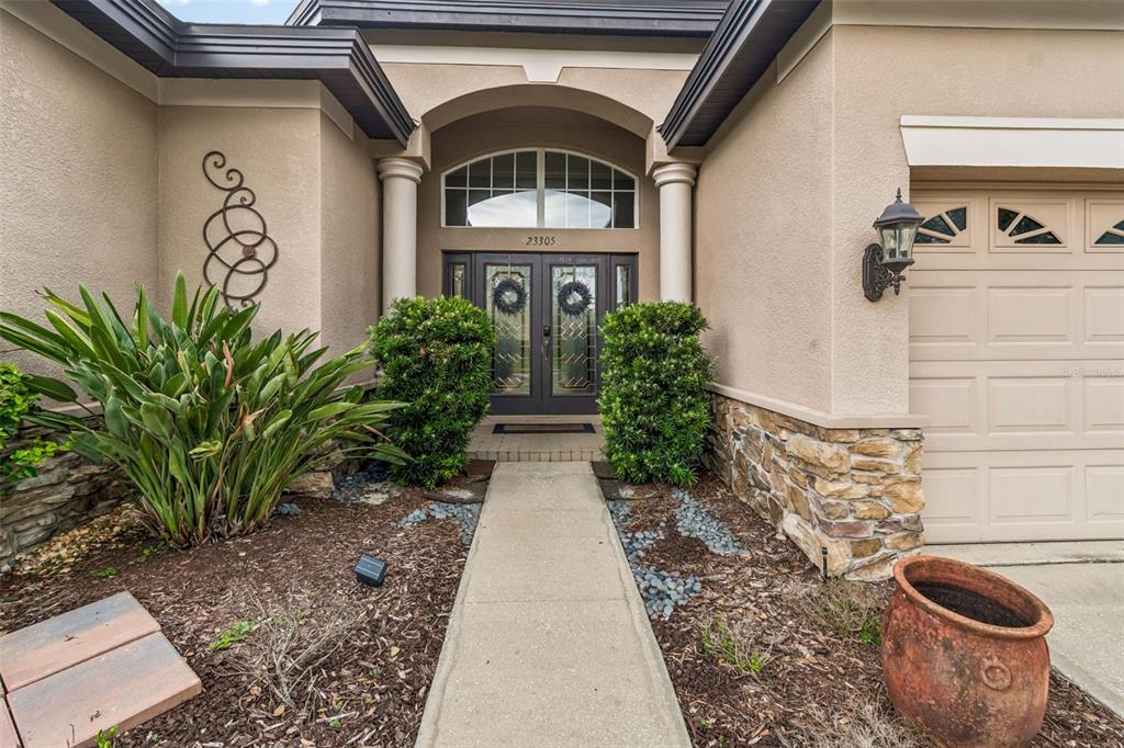 A concrete walkway leads to the front entrance of a house with a stone facade — 23305 GRACEWOOD CIRCLE, LAND O LAKES, FL