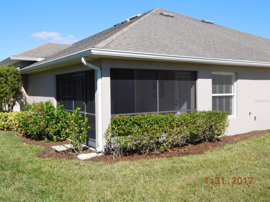 A beige house exterior features a screened-in porch, a single window, and landscaped bushes — 3670 LAKEWOOD BOULEVARD, NORTH PORT, FL