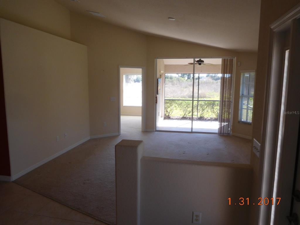 A living room with beige carpet, vaulted ceilings, and a sliding glass door to a lanai — 3670 LAKEWOOD BOULEVARD, NORTH PORT, FL