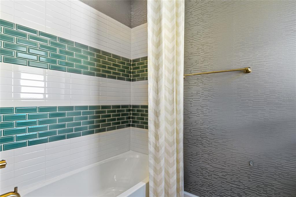 A bathroom features a white bathtub, green and white subway tile, and textured gray wallpaper — 207 THORNBERRY WAY, PALM COAST, FL