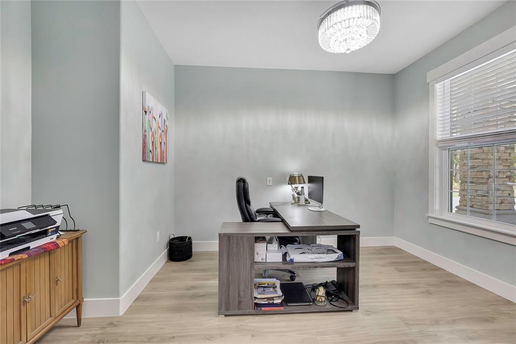 A home office features light blue walls, wood-look flooring, a desk, and a crystal chandelier — 3991 N BUCKHORN DRIVE, BEVERLY HILLS, FL