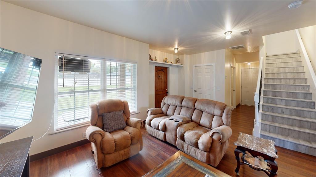 A living room features wood-look flooring, a brown recliner, a loveseat, and a staircase — 402 E MAPLE STREET, WINTER GARDEN, FL