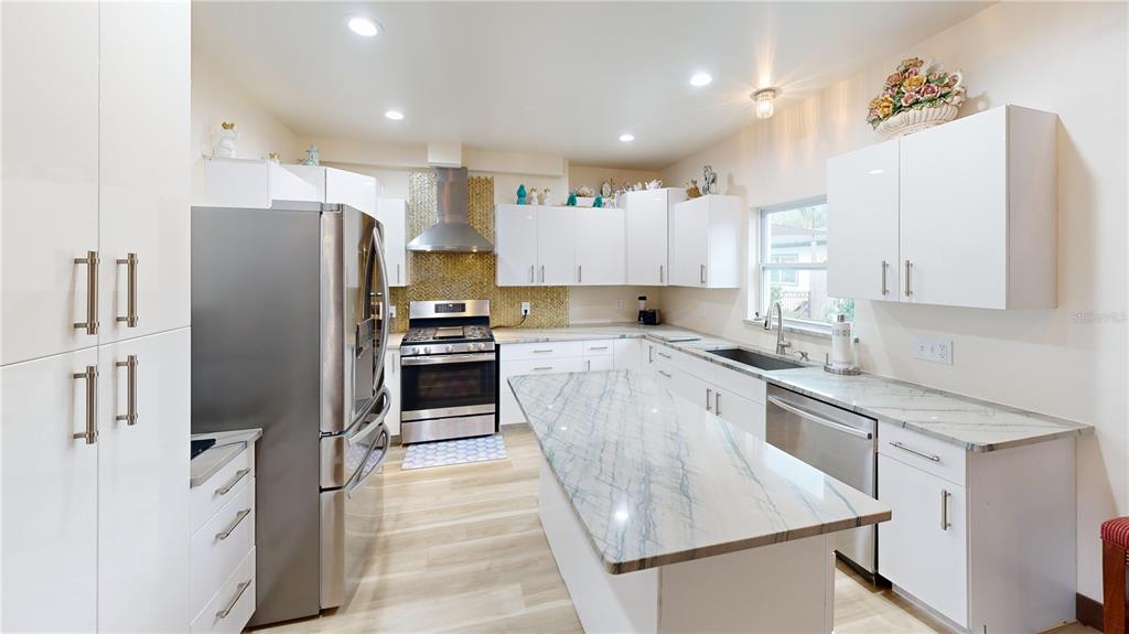 A modern kitchen features white cabinets, stainless steel appliances, and a marble-topped center island — 402 E MAPLE STREET, WINTER GARDEN, FL