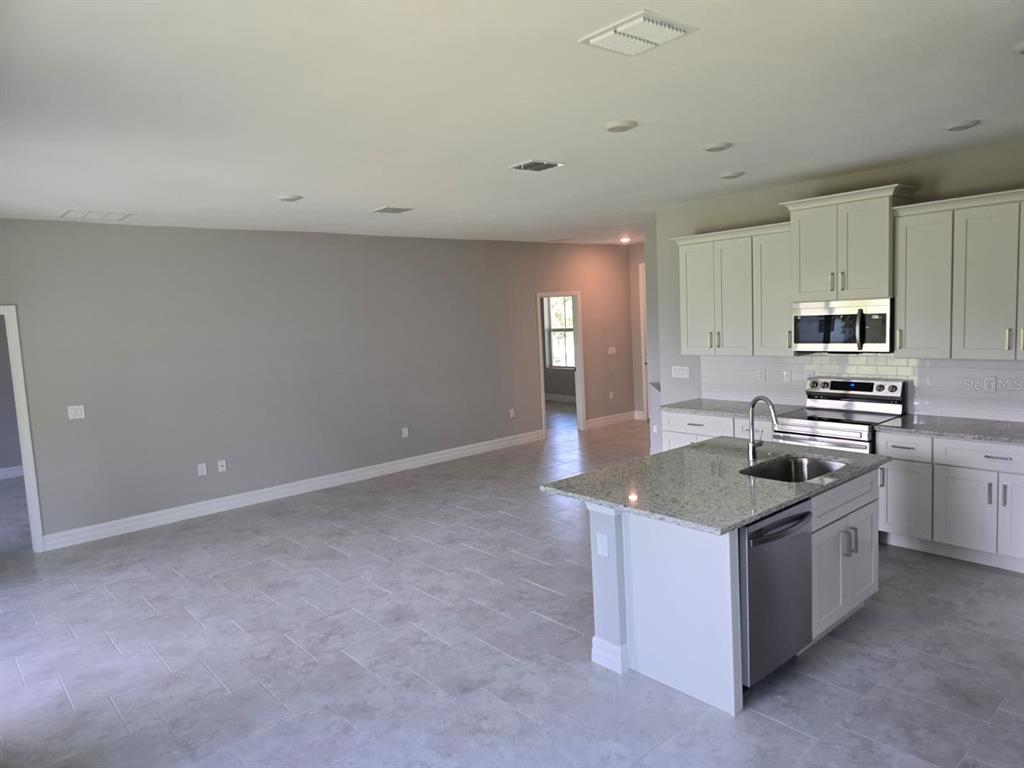 A kitchen with a granite island and light-colored cabinets opens into a large living area — 2857 SHADY AVENUE, NORTH PORT, FL