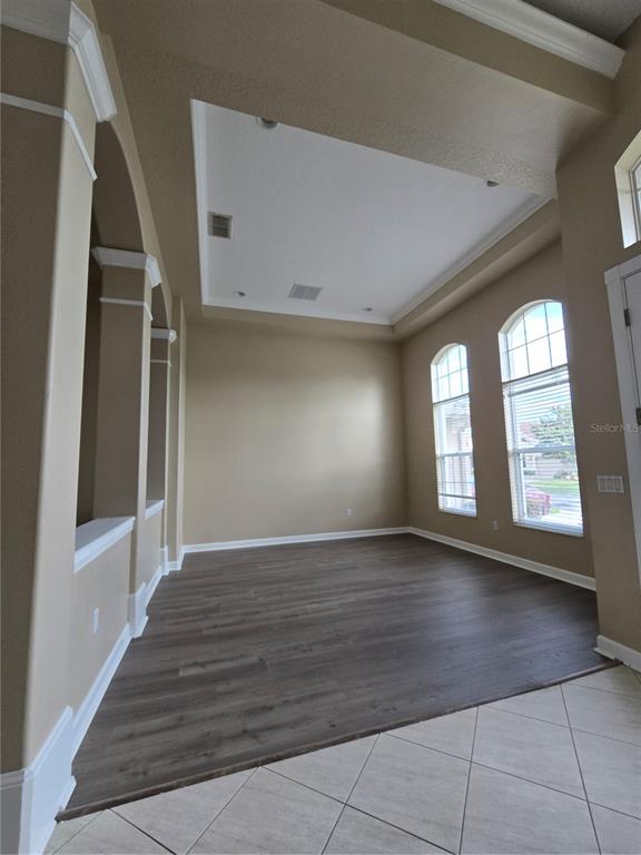 An empty room features a tray ceiling, dark wood-look flooring, and two arched windows — 13613 LARSEN LANE, WINTER GARDEN, FL