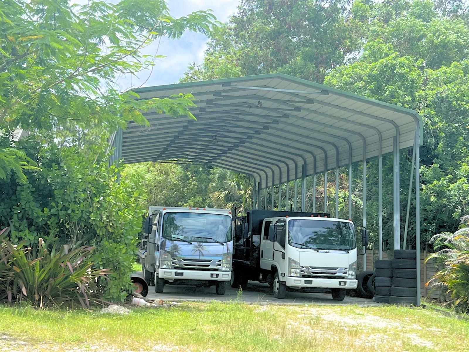 Two white trucks are parked under a large metal carport surrounded by lush green trees — 4811 N 122nd Dr Drive N, FL 33411, FL