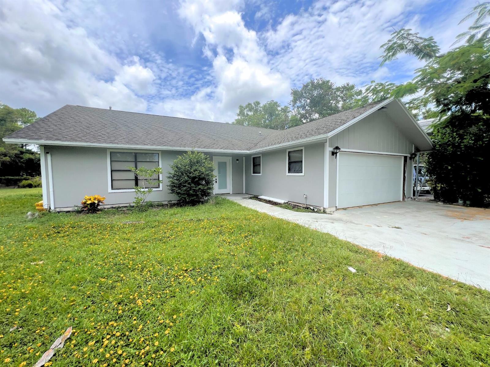 A single-story gray house with a two-car garage and a front lawn under a sky — 4811 N 122nd Dr Drive N, FL 33411, FL