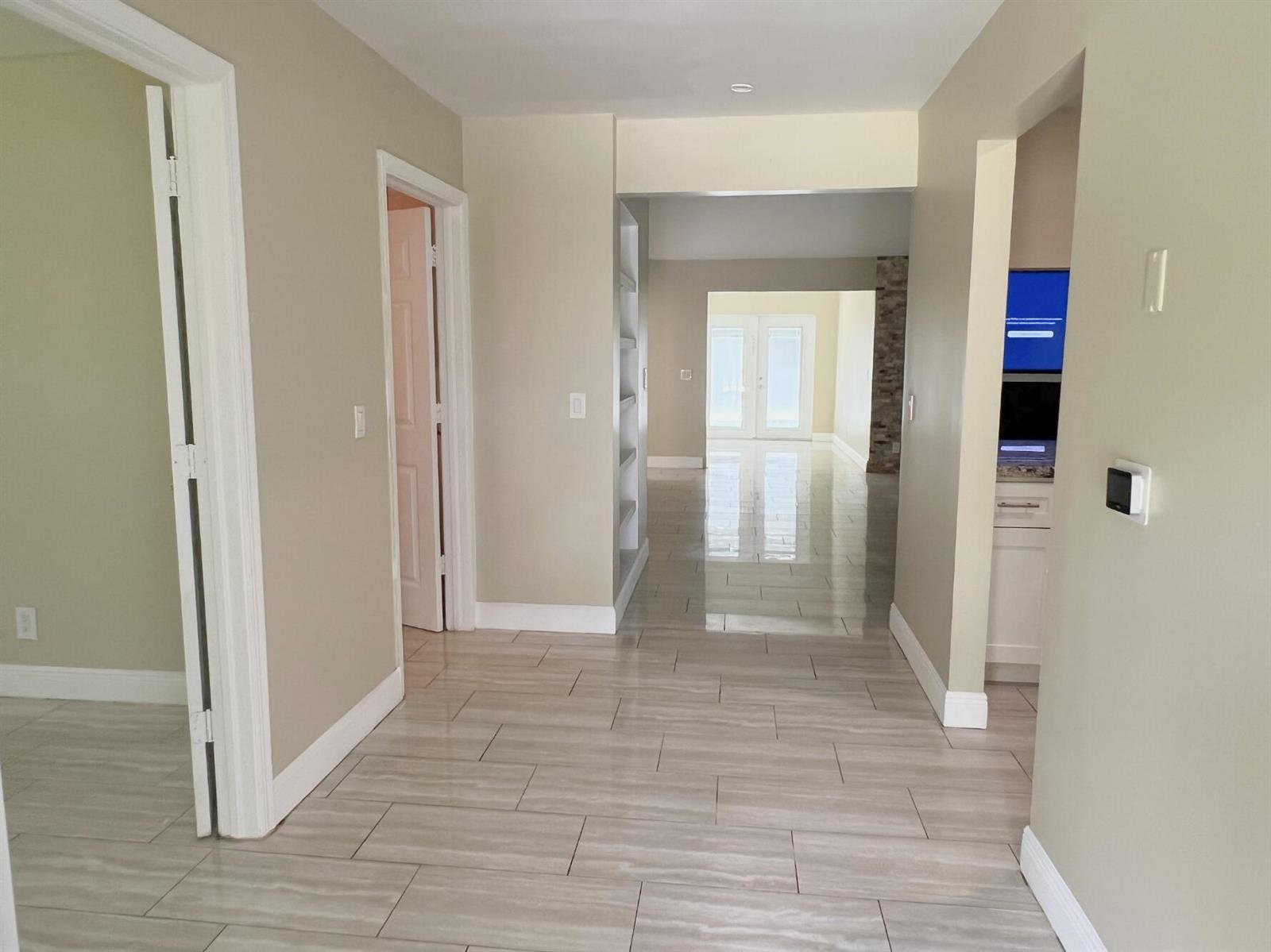 A hallway with light-colored tile flooring leads toward a bright living area with glass doors — 4811 N 122nd Dr Drive N, FL 33411, FL
