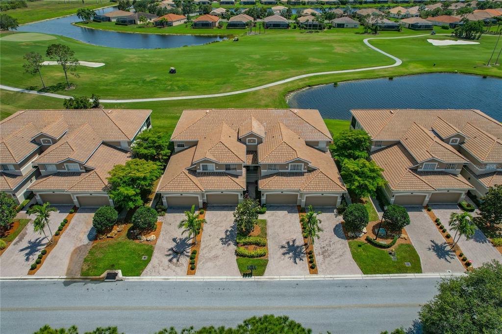 An aerial view shows a row of multi-unit townhomes with tile roofs facing a golf course — 8312 GRAND ESTUARY TRAIL UNIT 104, BRADENTON, FL