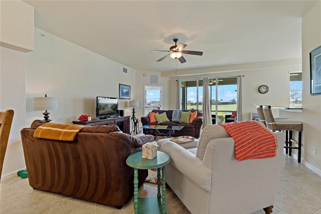 A living room features a brown sofa, a white armchair, and a sliding glass door — 8312 GRAND ESTUARY TRAIL UNIT 104, BRADENTON, FL