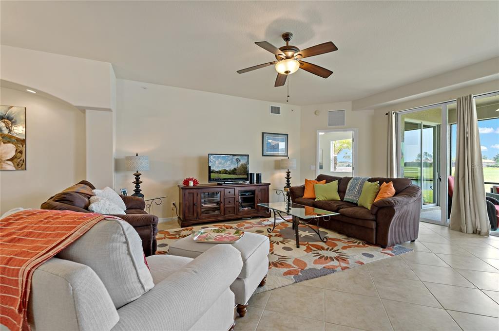A living room features tile floors, brown sofas, a ceiling fan, and sliding glass doors — 8312 GRAND ESTUARY TRAIL UNIT 104, BRADENTON, FL