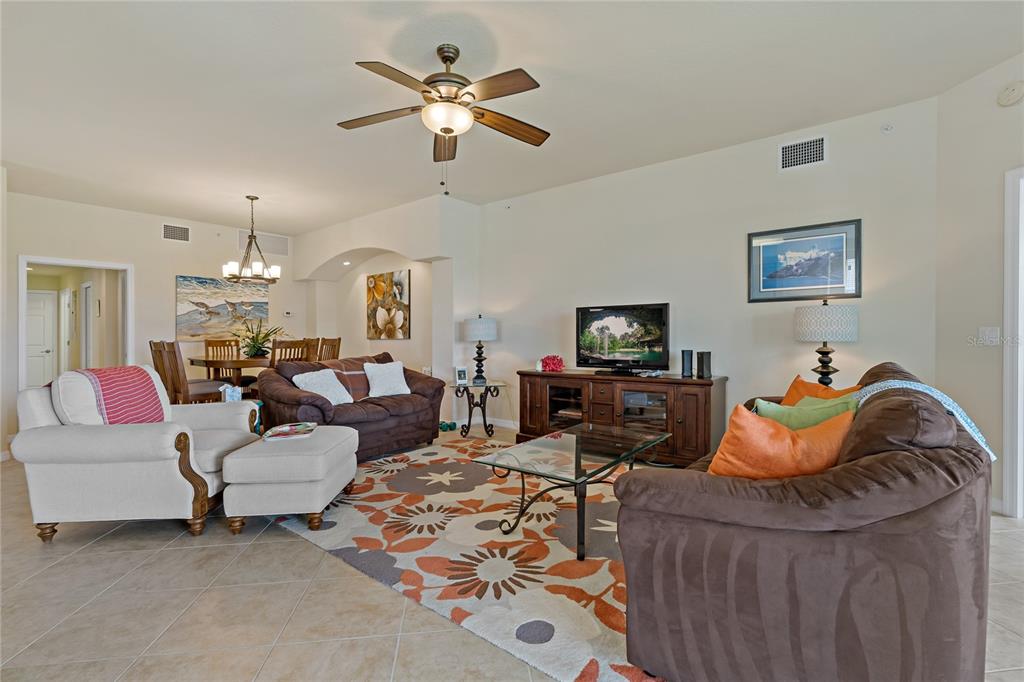 A living room features a ceiling fan, tile floors, a patterned rug, and brown sofas — 8312 GRAND ESTUARY TRAIL UNIT 104, BRADENTON, FL