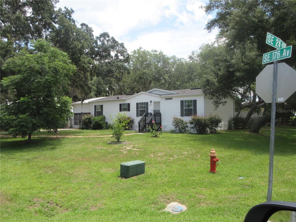 A white single-story house with dark shutters sits on a grassy lot with trees — 2391 SE 176TH AVENUE, SILVER SPRINGS, FL