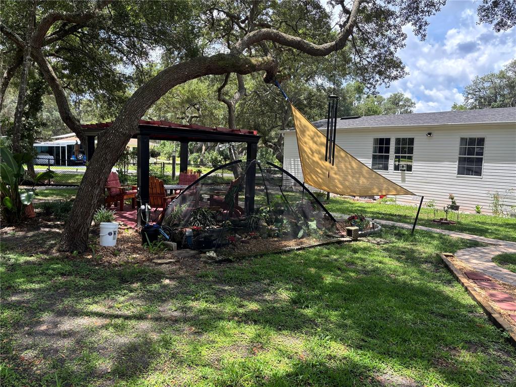 A backyard features a pergola, a mesh-covered garden bed, and a yellow shade sail — 2391 SE 176TH AVENUE, SILVER SPRINGS, FL