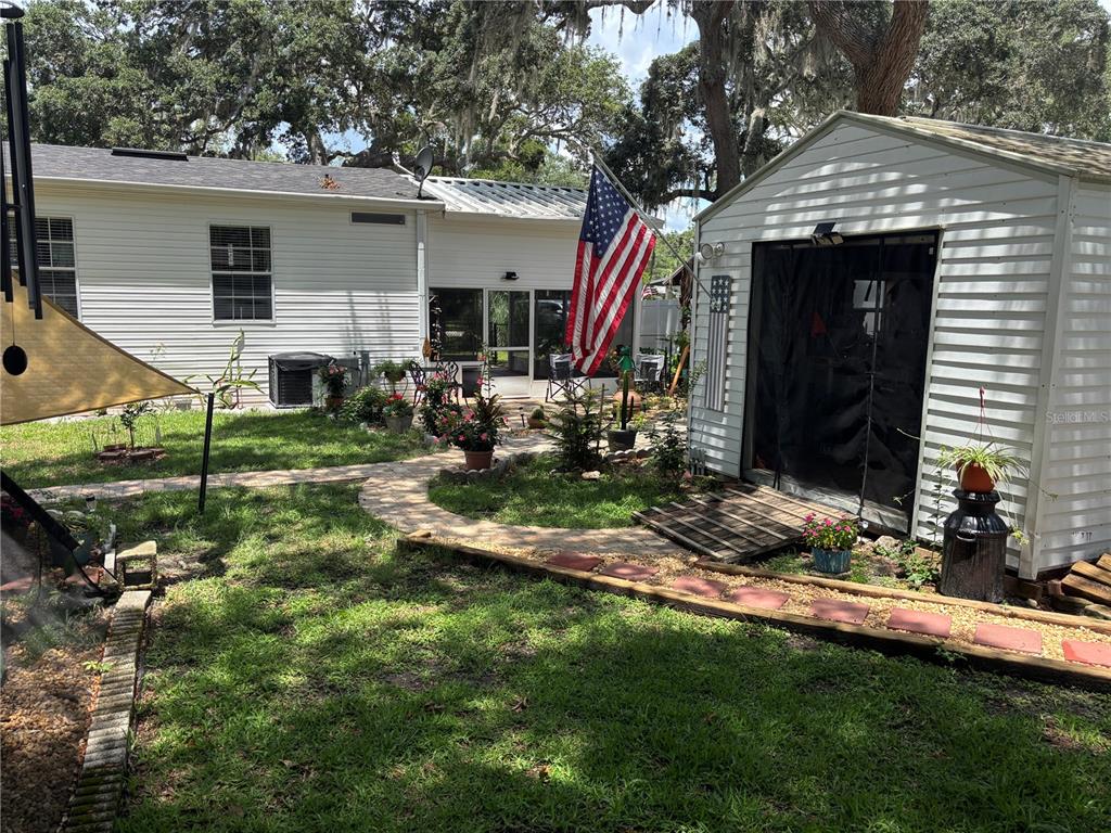 A backyard features a white house, a detached shed, a flag, and a stone walkway — 2391 SE 176TH AVENUE, SILVER SPRINGS, FL