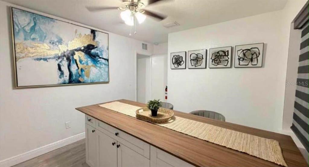 A dining area features a kitchen island with a wood countertop and abstract wall art — 6504 N PACKWOOD AVENUE, TAMPA, FL
