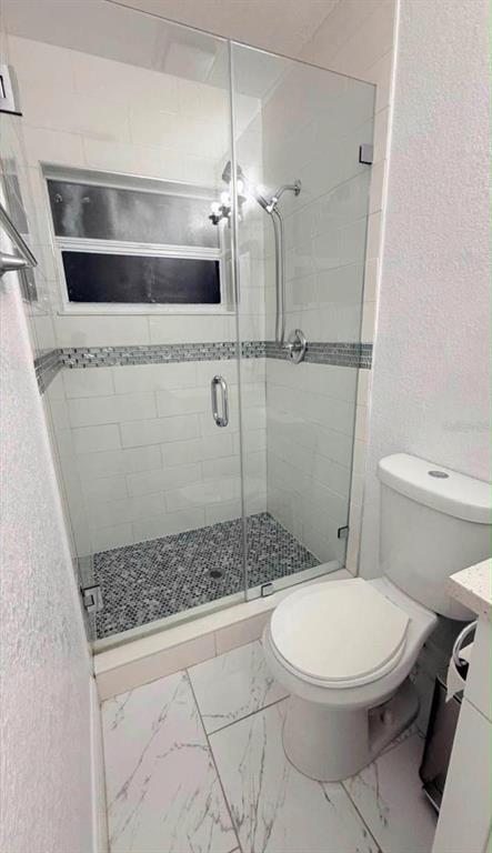 A bathroom features a glass-enclosed shower with tiled walls and a white toilet — 6504 N PACKWOOD AVENUE, TAMPA, FL