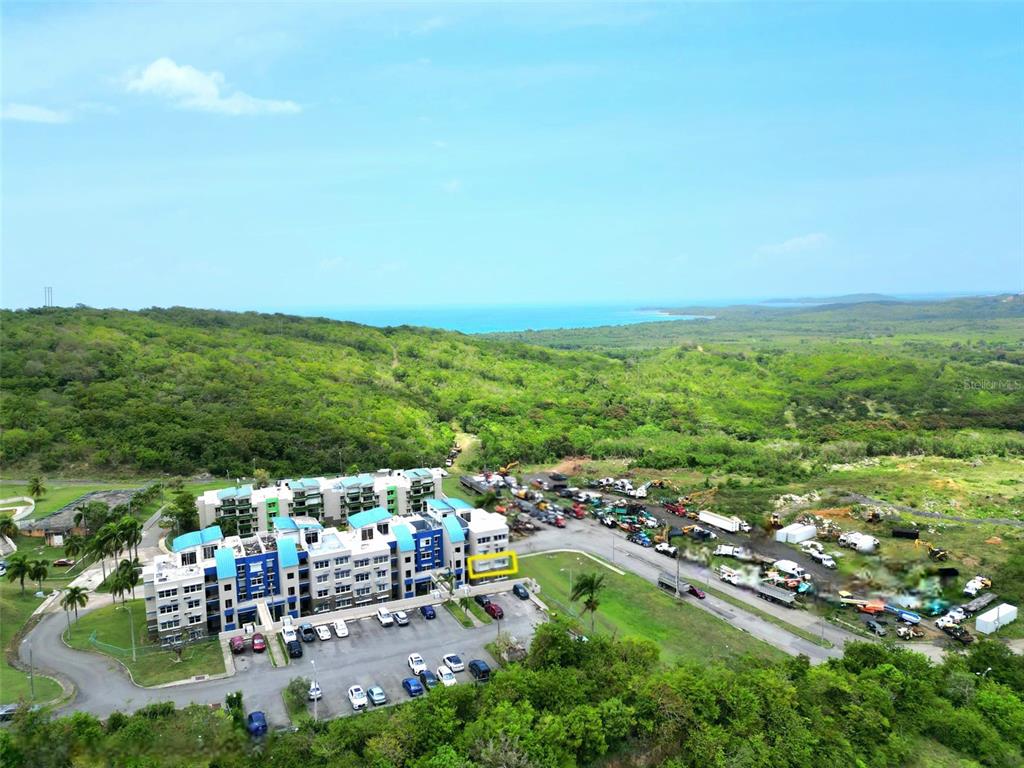 An aerial view shows a multi-story apartment building next to a construction equipment storage lot — 3 ST. MIRADOR PLAYA CONVENTO UNIT 10204, FAJARDO, PR