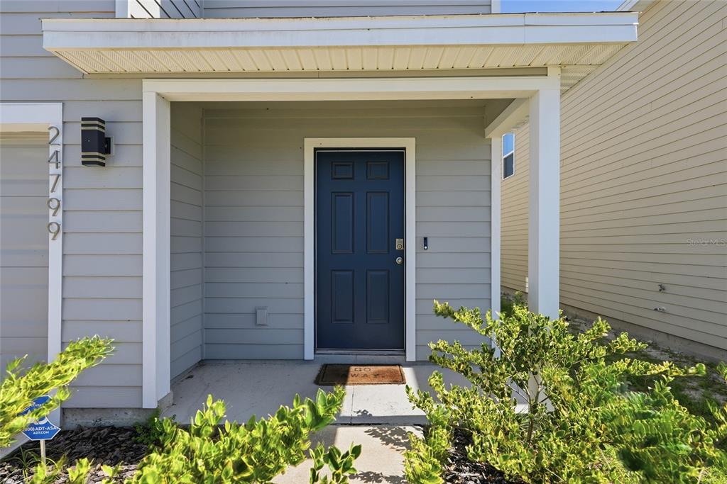 A blue front door is set within a covered porch of a light-gray house — 24799 NW 11TH PLACE, NEWBERRY, FL