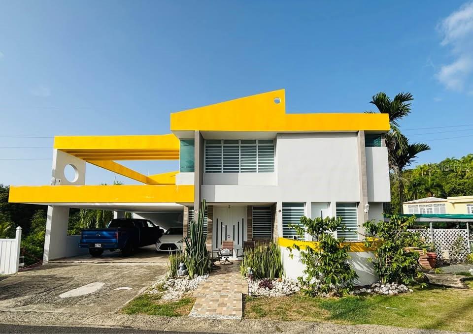 A modern two-story house with a bright yellow roofline, a carport, and a front walkway — Bo. Dajao Cam Los Oyola BO. DAJAO, BAYAMON, PR