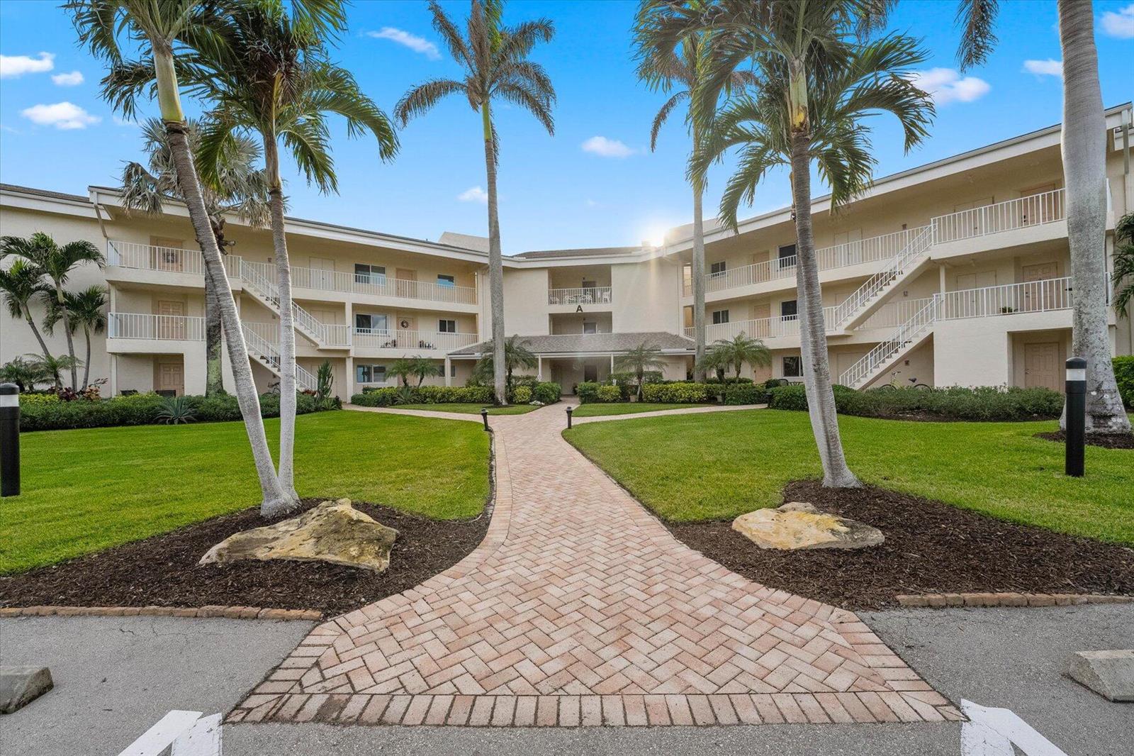 A brick walkway leads to the entrance of a three-story apartment building with palm trees — 2370 NE Ocean Boulevard # A203, Stuart FL 34996, STUART, FL