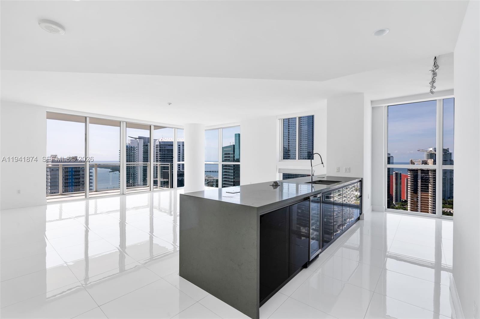 A modern kitchen island with dark cabinetry and gray countertops sits in a white room — 1080 Brickell Ave # 3901, Miami FL 33131, MIAMI, FL