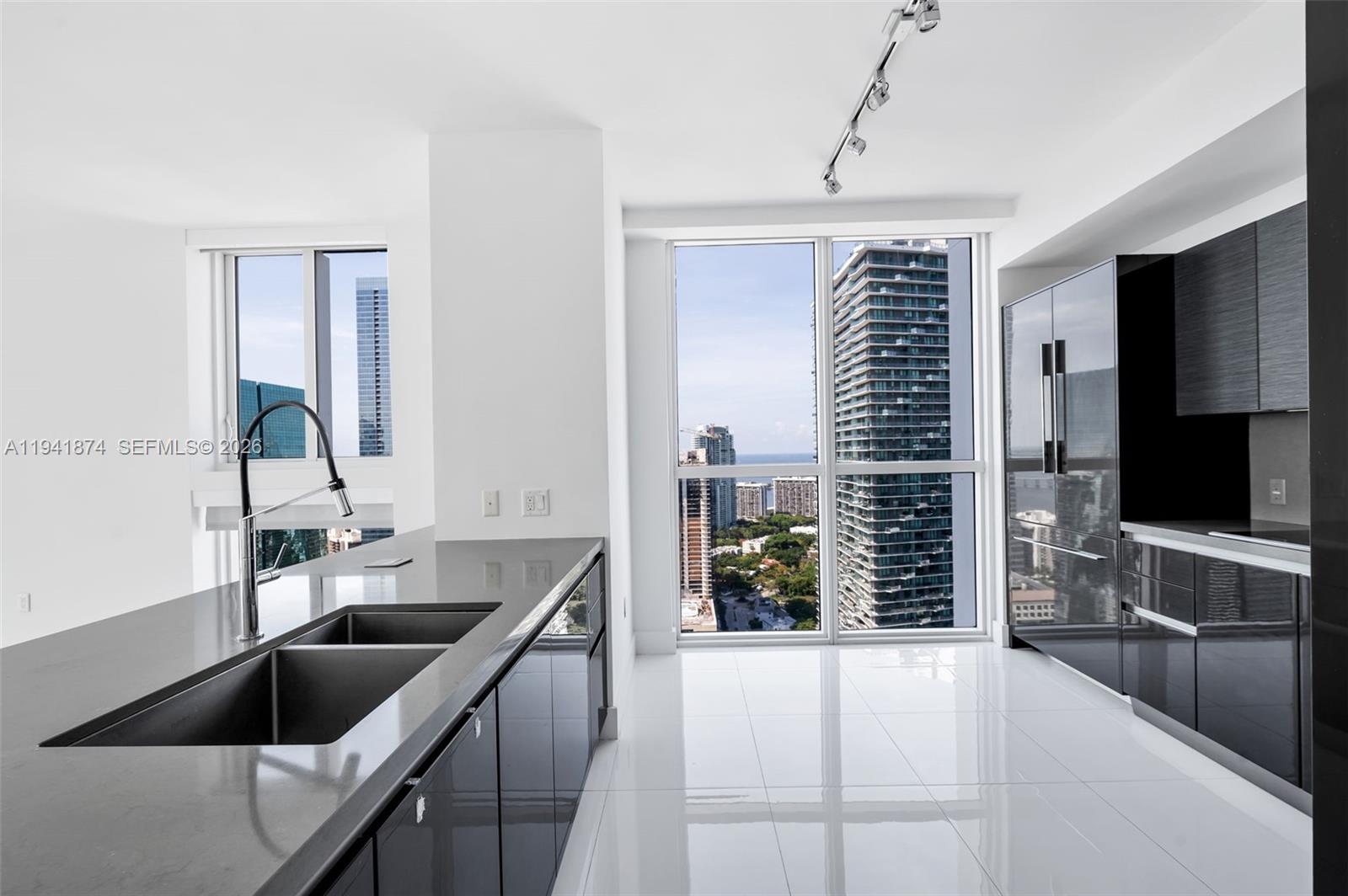 A modern kitchen features dark glossy cabinetry, gray countertops, and floor-to-ceiling windows with city views — 1080 Brickell Ave # 3901, Miami FL 33131, MIAMI, FL