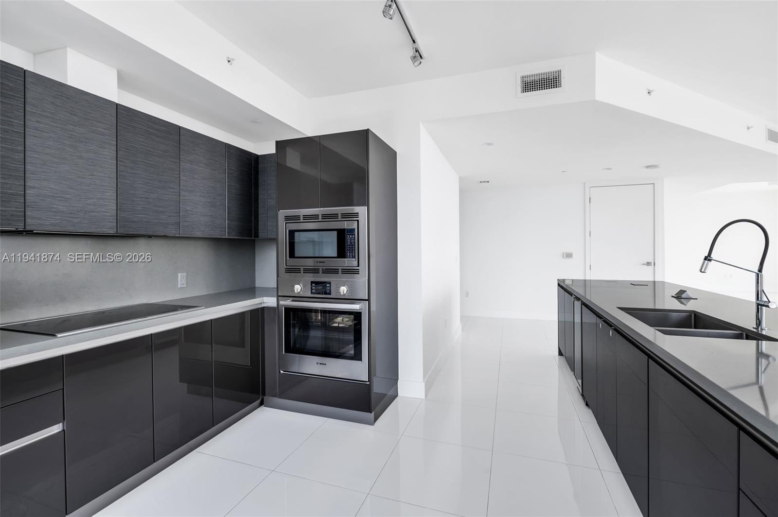 A modern kitchen features dark cabinetry, stainless steel appliances, and white tile flooring — 1080 Brickell Ave # 3901, Miami FL 33131, MIAMI, FL