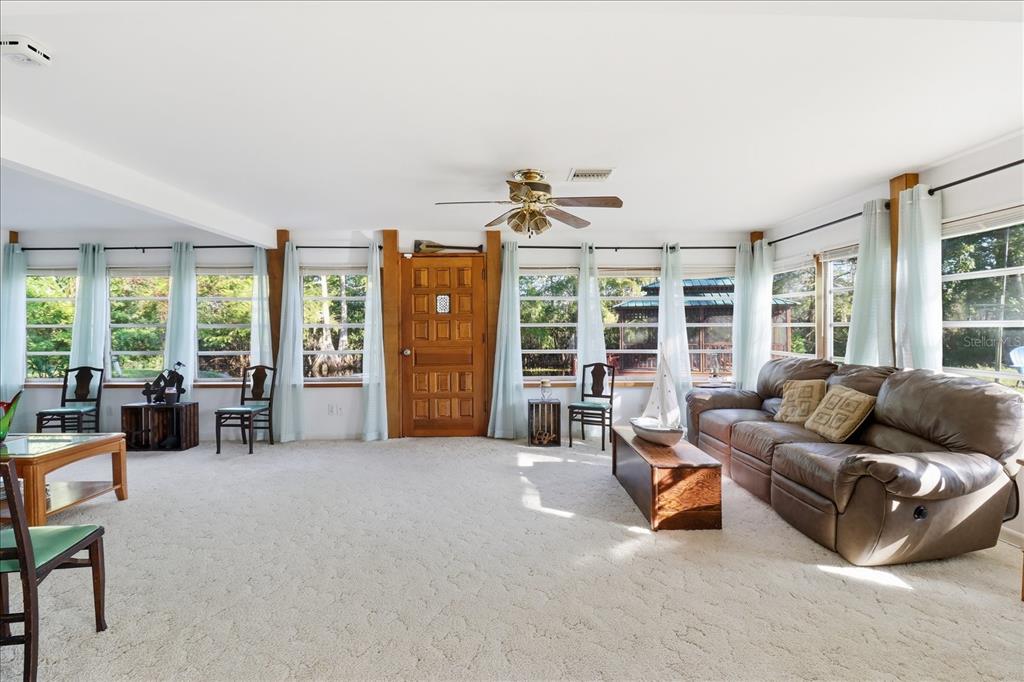 A living room with light carpet, a brown leather sofa, and many windows overlooking trees — 11641 E SALMON DRIVE, FLORAL CITY, FL