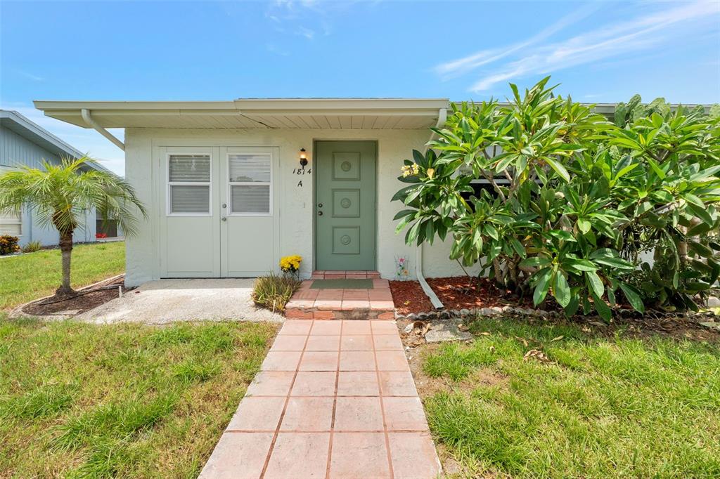 A single-story house with a green door, a paved walkway, and a covered carport — 1814 FOXHUNT DRIVE UNIT A, SUN CITY CENTER, FL
