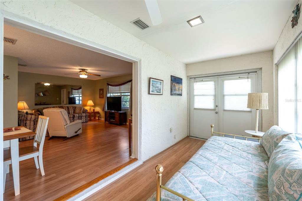 A sunroom with a daybed opens into a living room featuring wood-look flooring and furniture — 1814 FOXHUNT DRIVE UNIT A, SUN CITY CENTER, FL