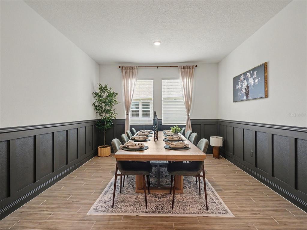 A dining room features dark wainscoting, a long wooden table, and light-colored wood-look flooring — 7474 SEA MANATEE STREET, PARRISH, FL