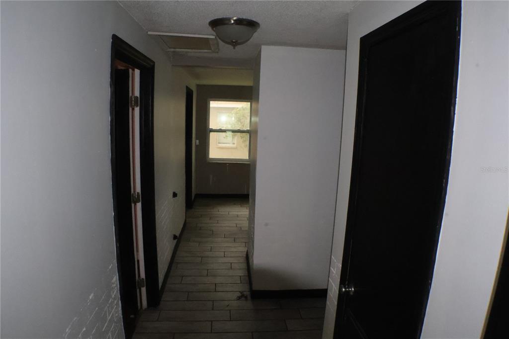 A hallway with gray tile flooring, white walls, and black door frames leads to a window — 1202 N FERRELL STREET, PLANT CITY, FL