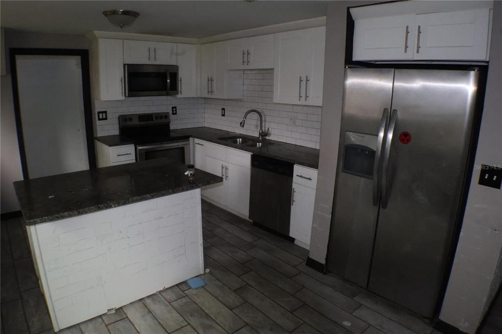 A kitchen features white cabinets, stainless steel appliances, dark countertops, and gray wood-look tile flooring — 1202 N FERRELL STREET, PLANT CITY, FL