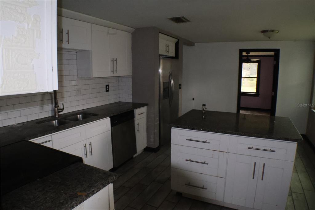 A kitchen features white cabinets, dark countertops, a center island, and stainless steel appliances — 1202 N FERRELL STREET, PLANT CITY, FL