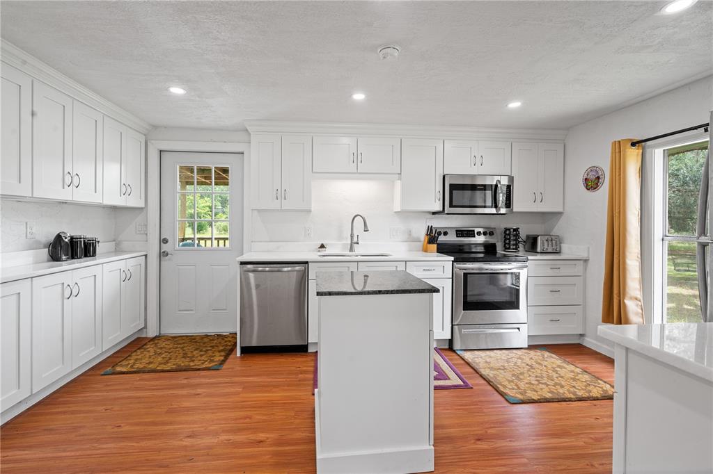 A kitchen features white cabinets, stainless steel appliances, a center island, and wood-look flooring — 6850 SE 192ND COURT, MORRISTON, FL
