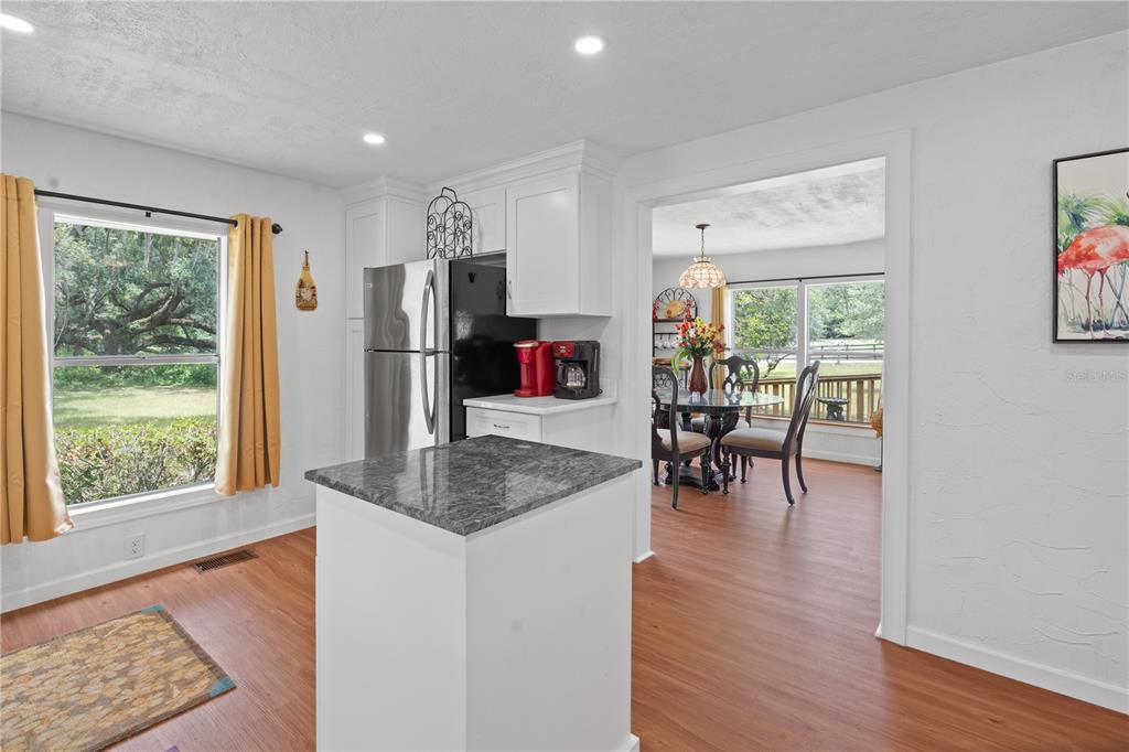 A kitchen with white cabinets, a granite-topped island, and a view into a dining area — 6850 SE 192ND COURT, MORRISTON, FL
