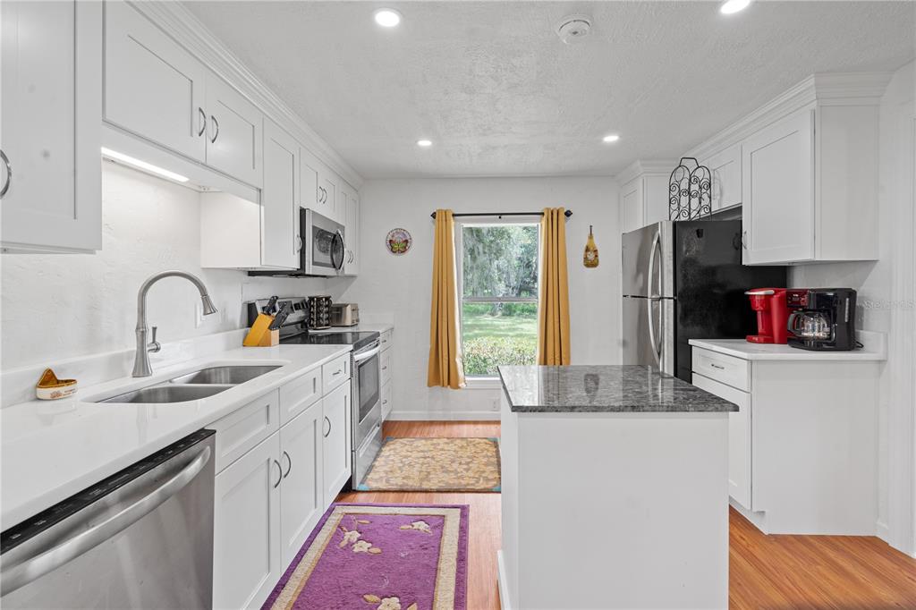 A kitchen with white cabinets, stainless steel appliances, a granite-topped island, and a window view — 6850 SE 192ND COURT, MORRISTON, FL