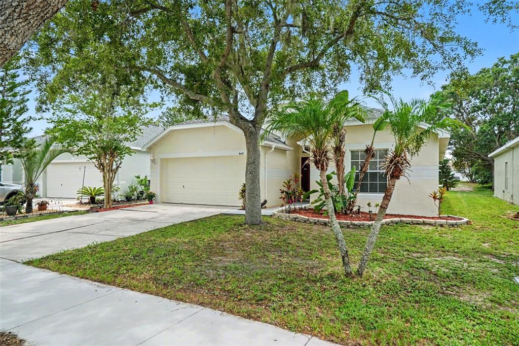 A single-story house with a two-car garage, a paved driveway, and mature trees in front — 9407 CYPRESS HARBOR DRIVE, GIBSONTON, FL