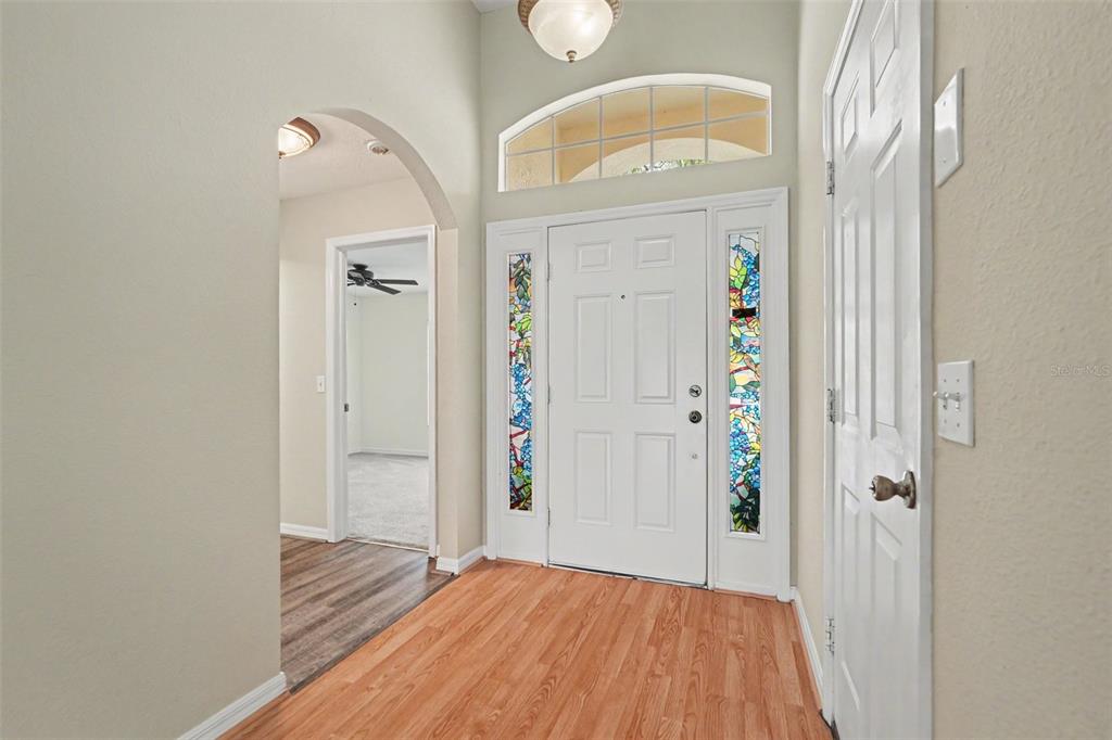An entryway features a white front door with stained glass sidelights, wood flooring, and an archway — 9407 CYPRESS HARBOR DRIVE, GIBSONTON, FL