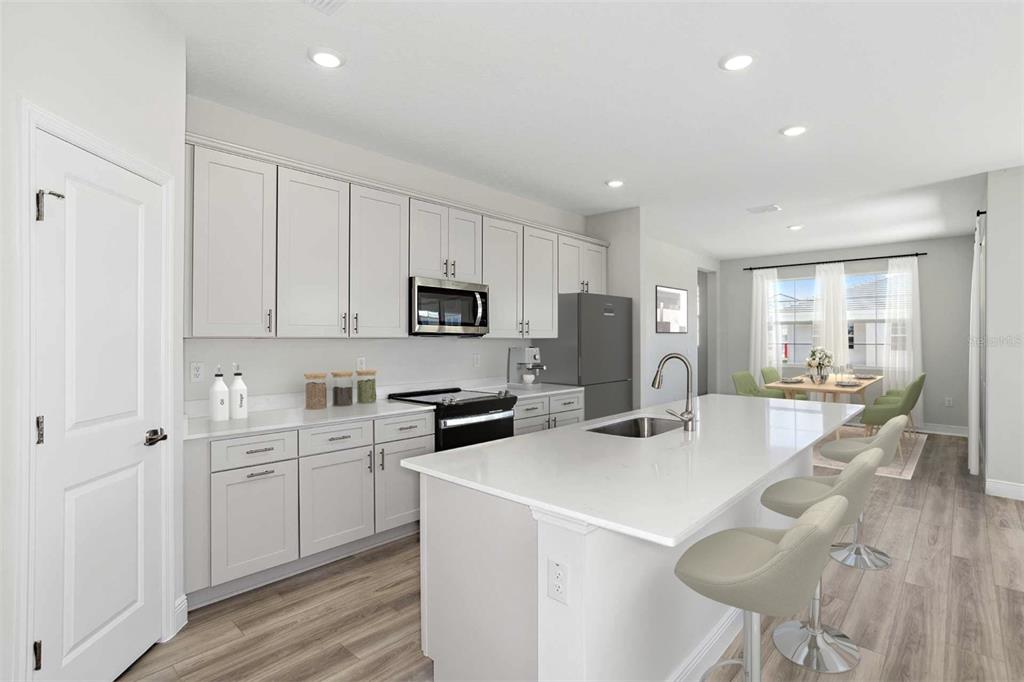 A modern kitchen features light gray cabinets, white countertops, a central island, and stainless appliances — 33595 TWILIGHT SEA PLACE, DADE CITY, FL